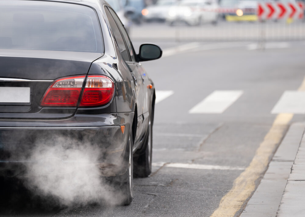 Person wearing gloves testing or inspecting car exhaust emissions on a street using specialized equipment. 